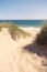 A sandy path through the dunes and grass leading to the beach on the Cape Cod National Seashore on a blue sky summer day. Waves are visible in the blue ocean and green grasses are growing on a hot day