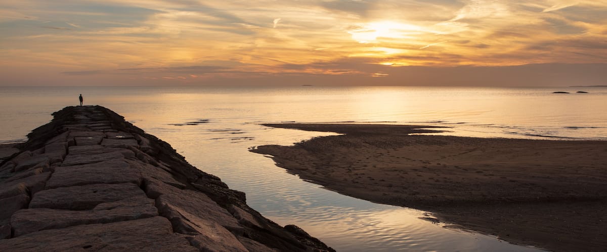 A silhouette of a man standing on a jetty looking at the sunset.