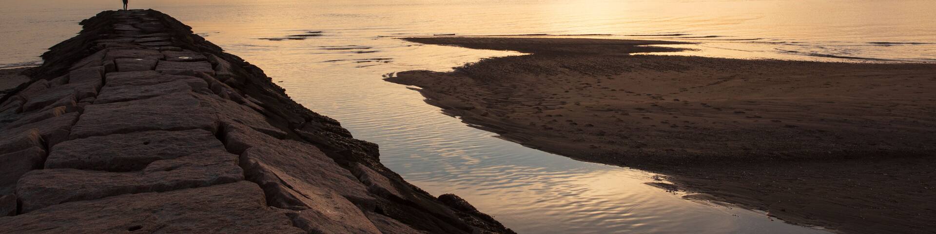 A silhouette of a man standing on a jetty looking at the sunset.