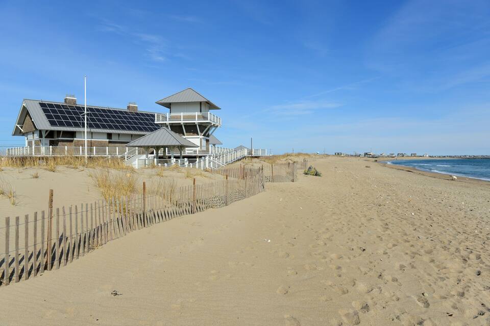 Une maison de plage dotée de panneaux solaires, d’une clôture en bois et située sur une plage de sable.