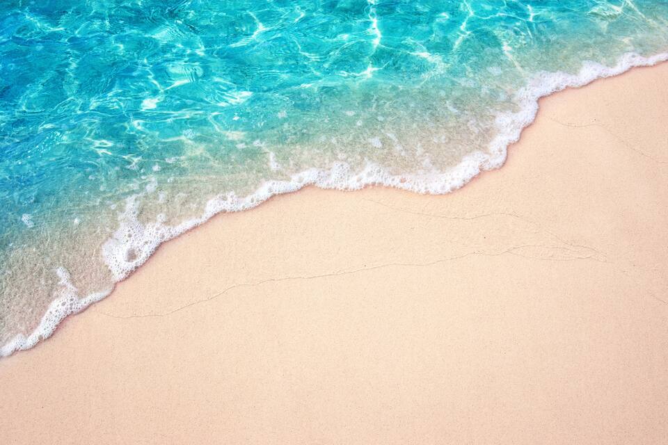 Une plage de sable fin bordée d’une eau turquoise et limpide, où les vagues se brisent doucement.
