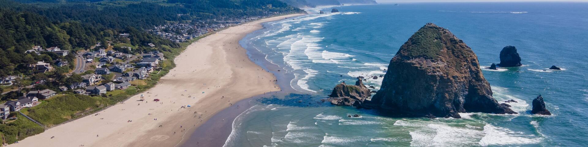 A coastal town with a beach, ocean waves, and mountains in the background.