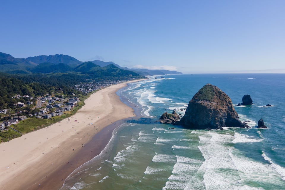 A coastal town with a beach, ocean waves, and mountains in the background.