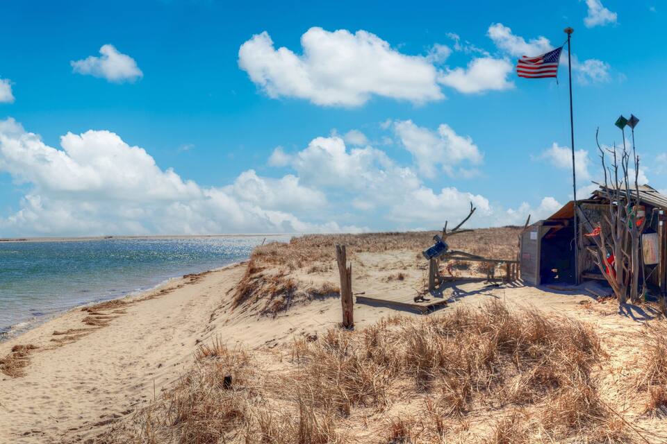 En strand med en liten träkonstruktion, en flagga och en klarblå himmel.