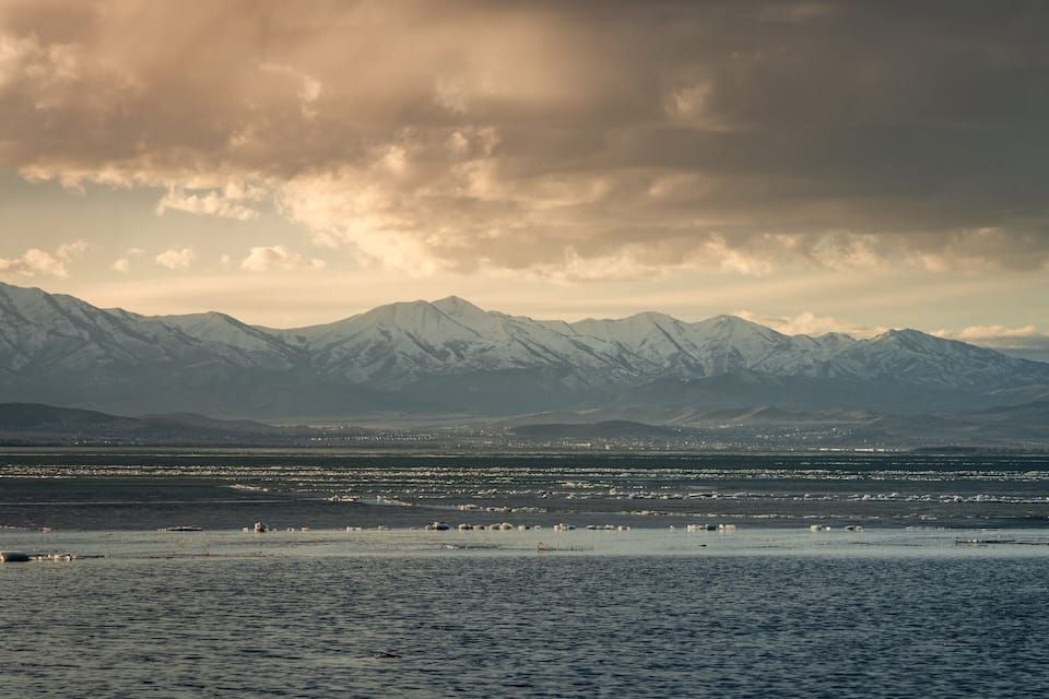 A mountain range with snow-capped peaks and a body of water in the foreground.