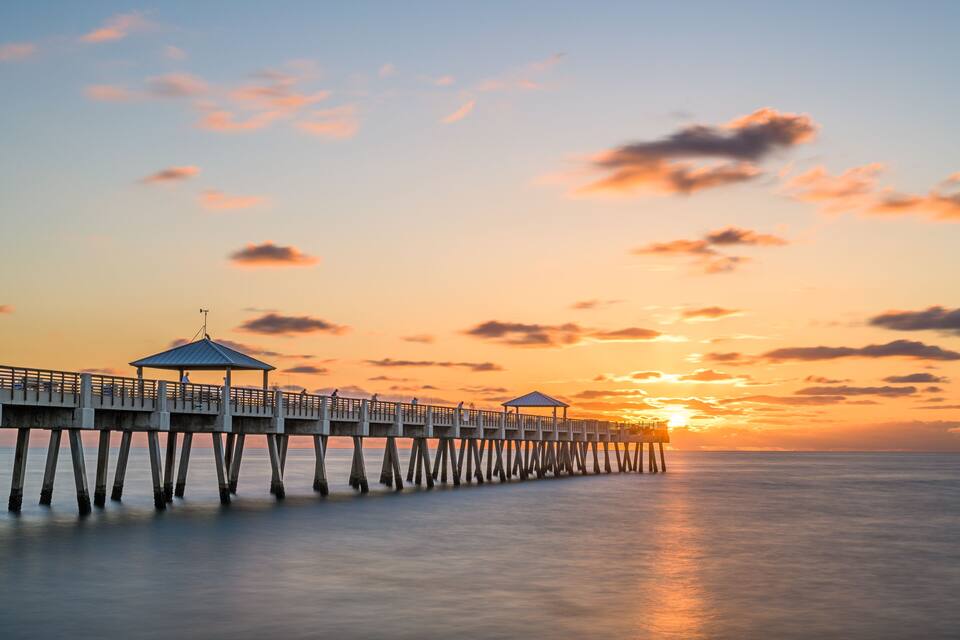 A pier extending into calm waters at sunset with a clear sky.