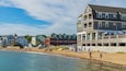 A beach with people, a wooden pier, and buildings in the background.