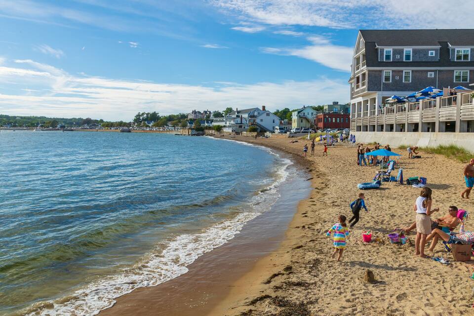 A beach with people, umbrellas, and beach chairs.