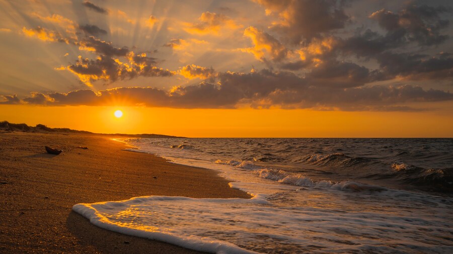 Sunrise seascape and cloudscape over the white foam waves rolling in on the beach at South Cape Beach in Mashpee, Massachusetts