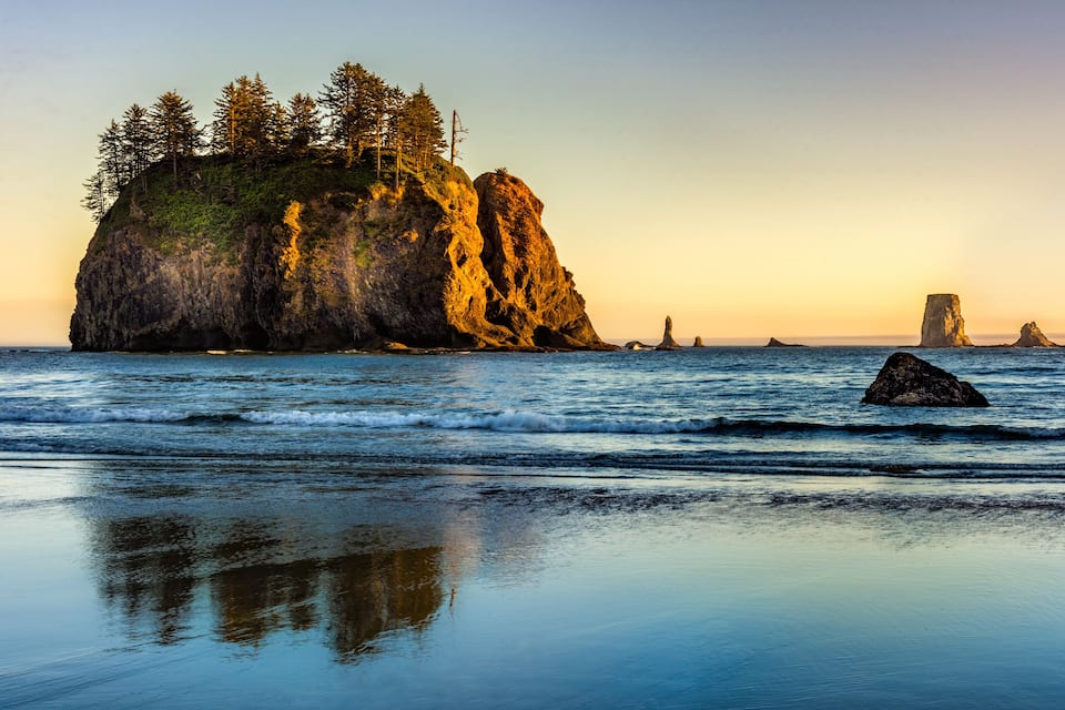A rocky coastline with trees, calm waves, and clear skies.