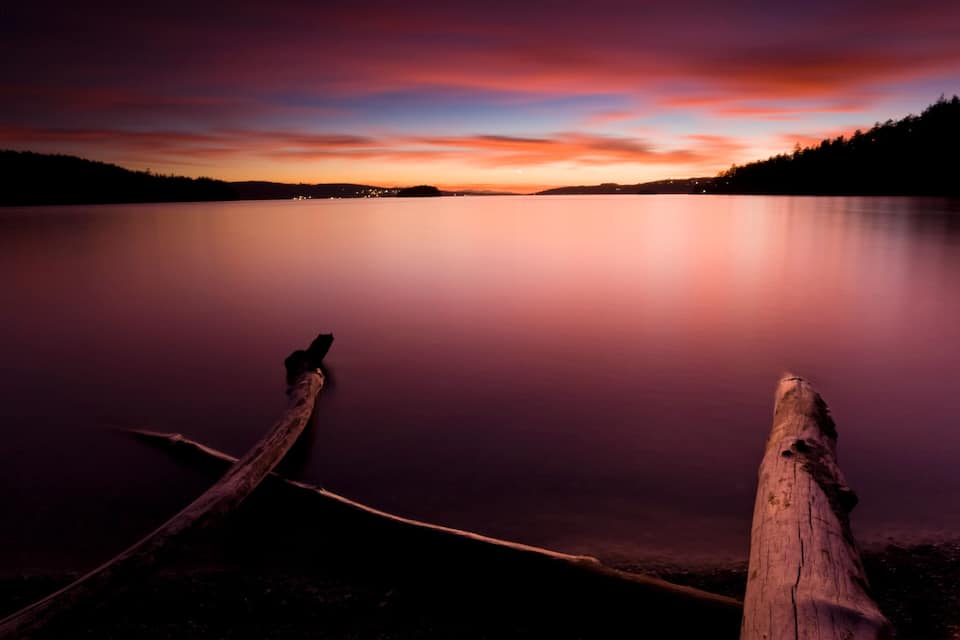 A calm lake at sunset with a wooden dock extending into the water.