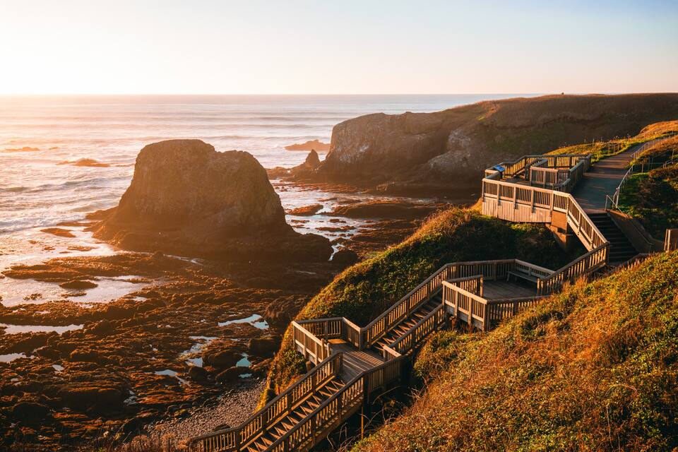 A coastal landscape with rocky cliffs and wooden staircases leading down to the beach.