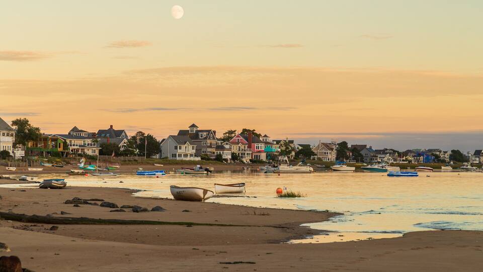 A beach with boats, houses, and a moon in the sky.