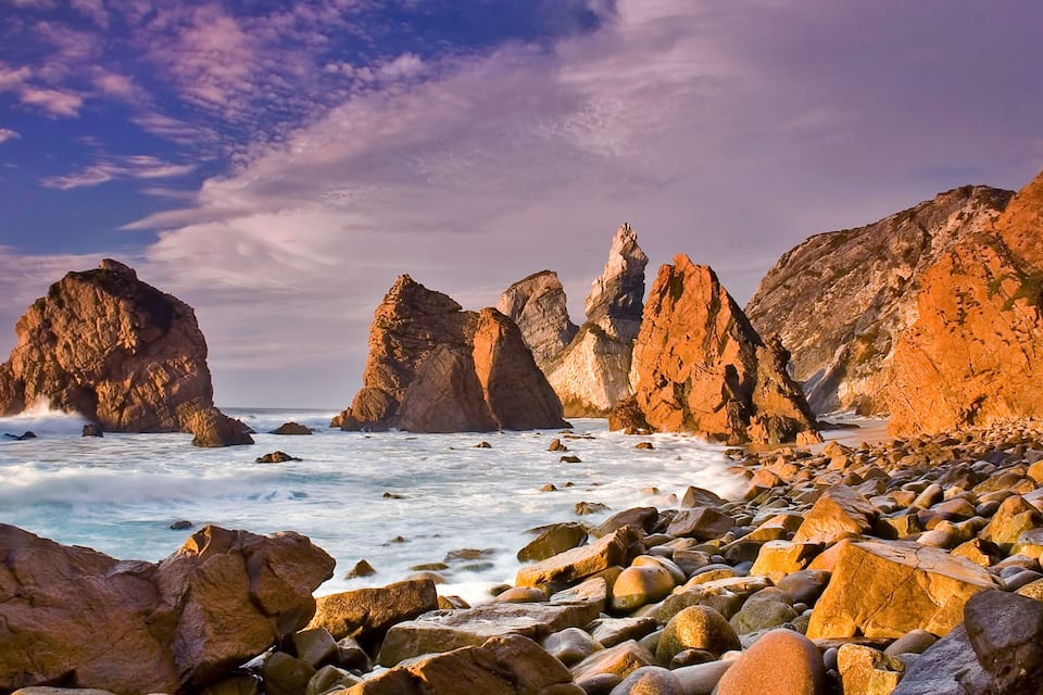 A rocky coastline with large boulders and cliffs under a partly cloudy sky.