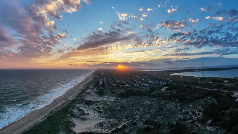 A coastal sunset with a beach, ocean waves, and a road leading to a distant town.