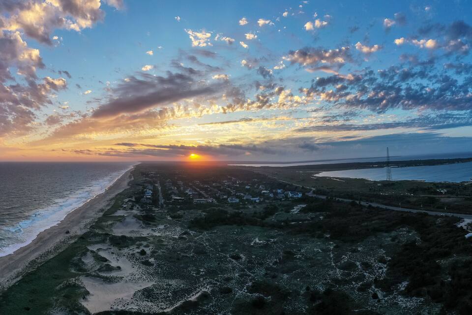 A coastal sunset with a beach, ocean waves, and a road leading to a distant town.