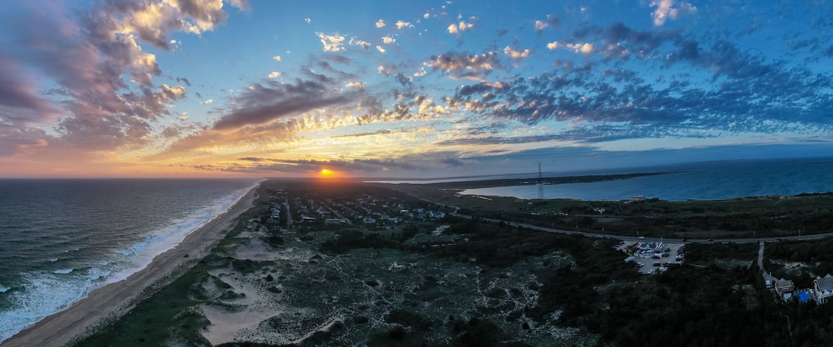 A coastal sunset with a beach, ocean waves, and a road leading to a distant town.