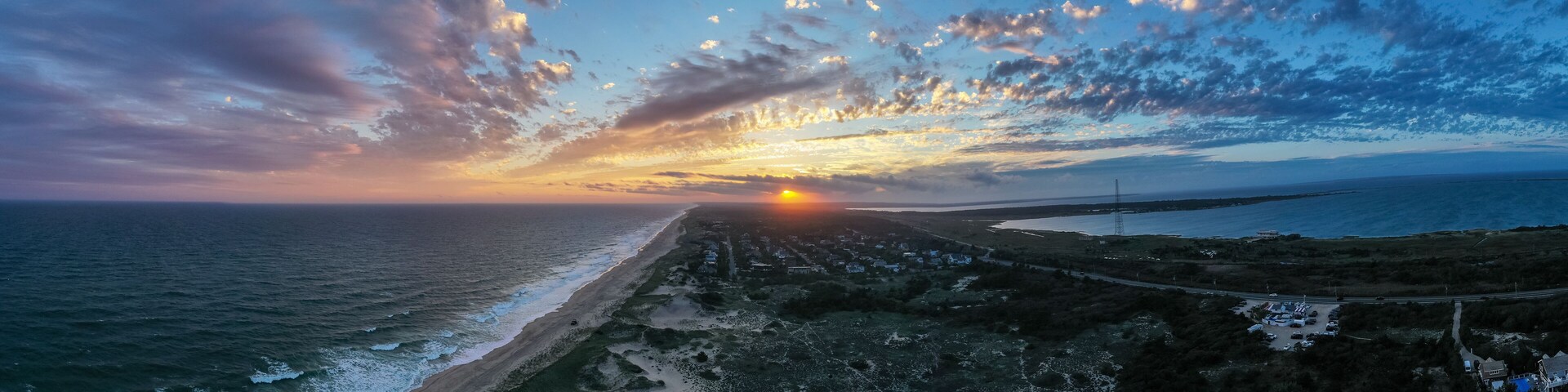 A coastal sunset with a beach, ocean waves, and a road leading to a distant town.
