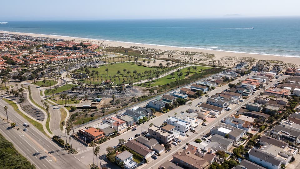 A coastal residential area with a beach, a park with palm trees, and a clear view of the ocean.