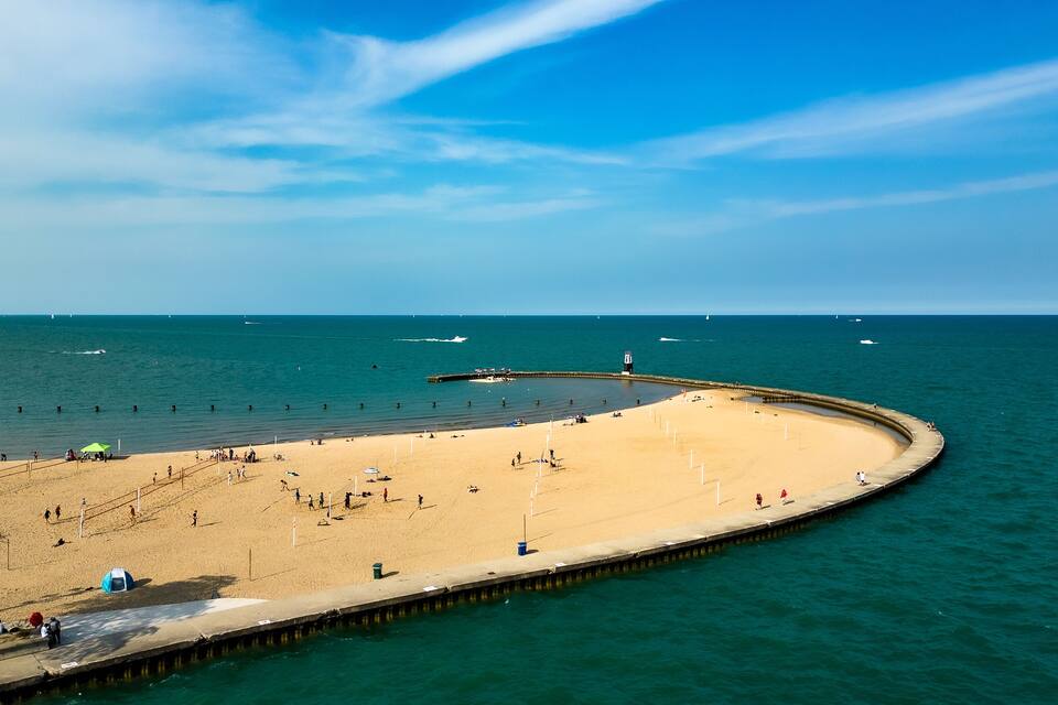 Una spiaggia sabbiosa con un molo curvo che si protende nel mare, immersa in acque calme e sotto un cielo sereno.