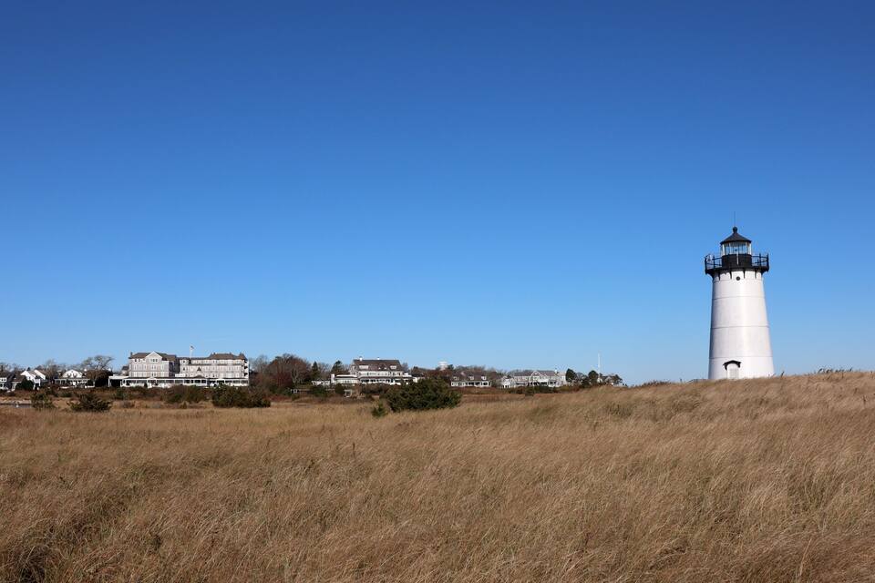 A white lighthouse on a hill with a clear blue sky.