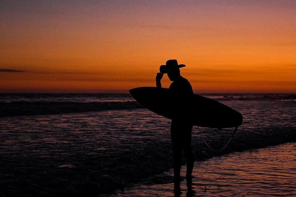 A silhouette of a person holding a surfboard at sunset.