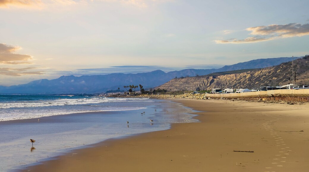 a stunning panoramic shot of the vast blue ocean at the beach with smooth silky brown sand and rocks along the beach at sunset with powerful clouds at Rincon Beach in Ventura County California USA