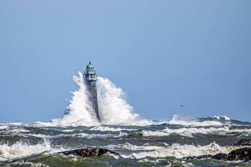 A lighthouse amidst rough seas with waves crashing against it.