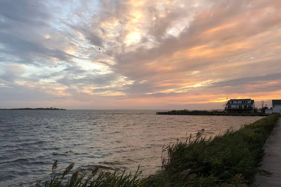 A coastal sunset with a wooden pier and a white house.