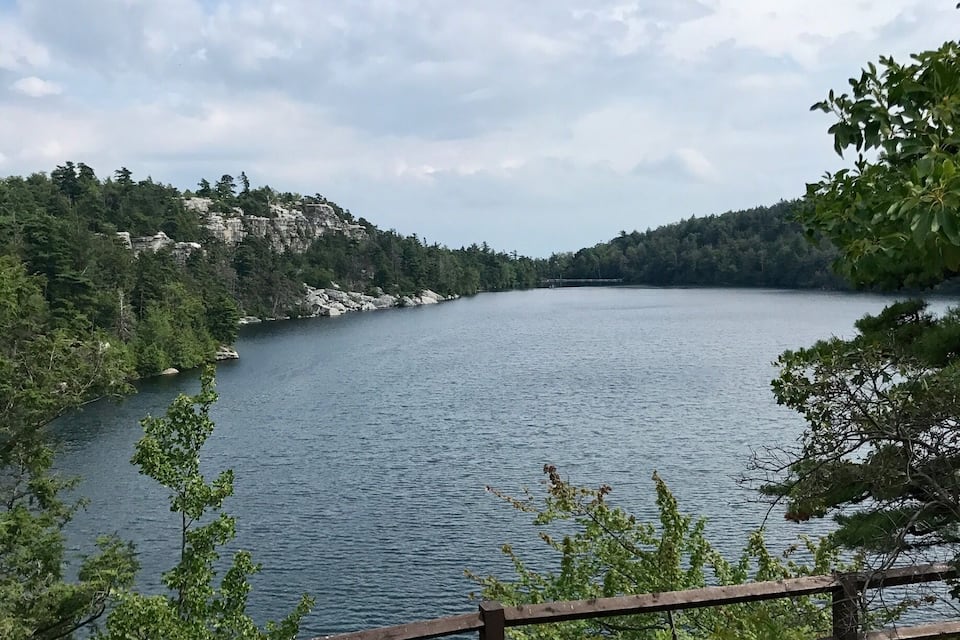 A lake surrounded by forested hills and a wooden fence.