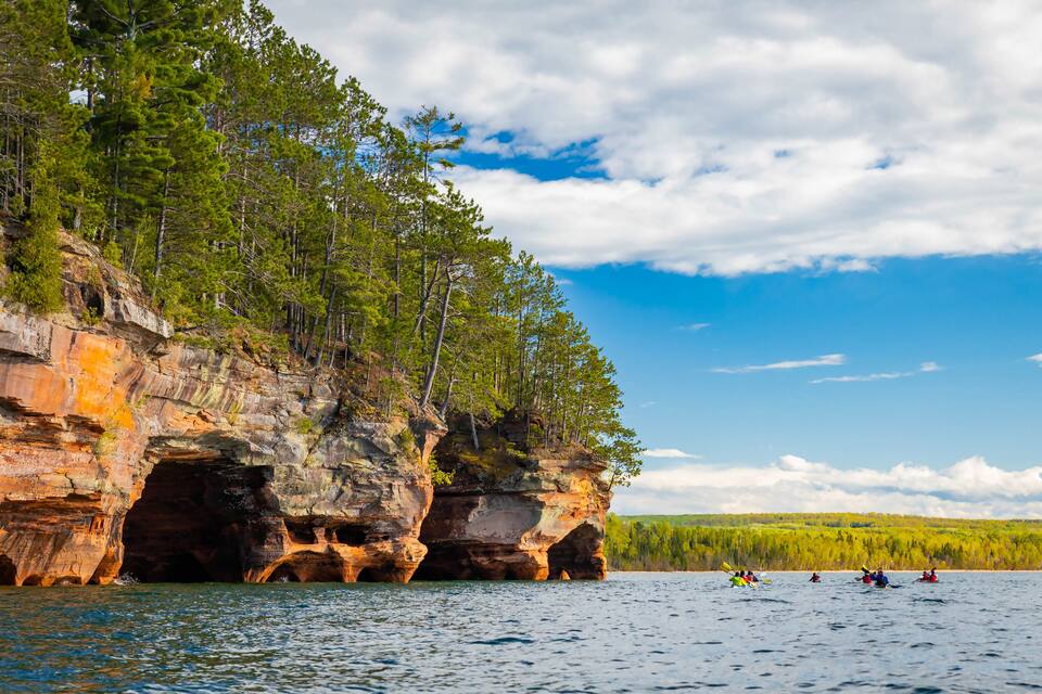 En stejl klippe med skov og kajakroere på vandet.
