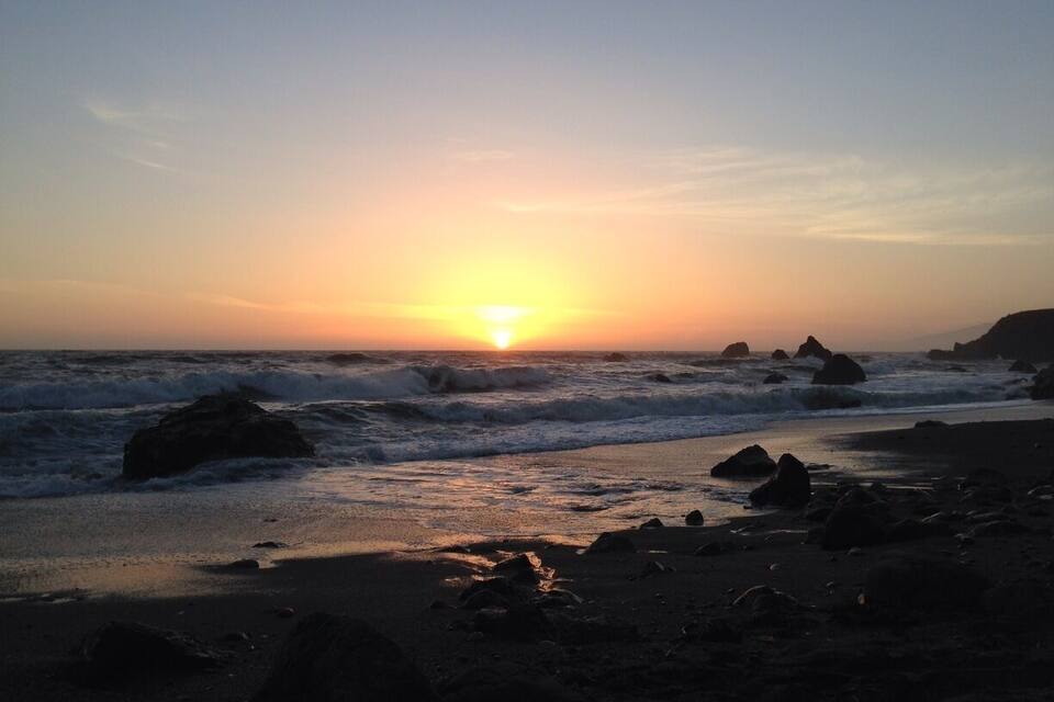 A sunset over a rocky beach with waves crashing onto the shore.