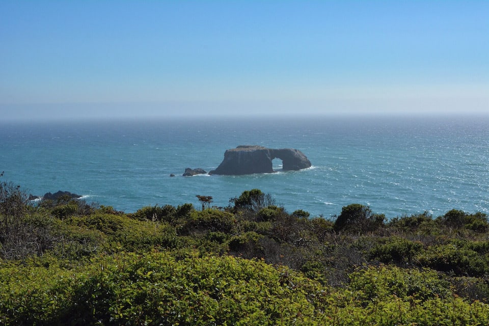 Un paisaje costero con una formación rocosa destacada en el mar, rodeado de abundante vegetación.