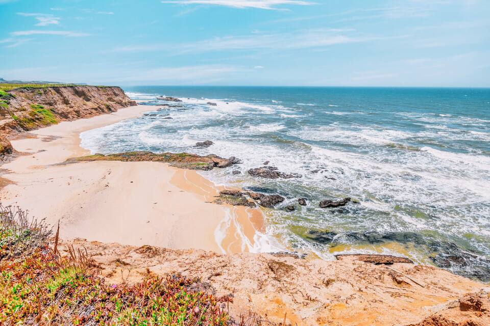 Paisatge costaner amb una platja sorrenca, roca a la riba i ones oceàniques.