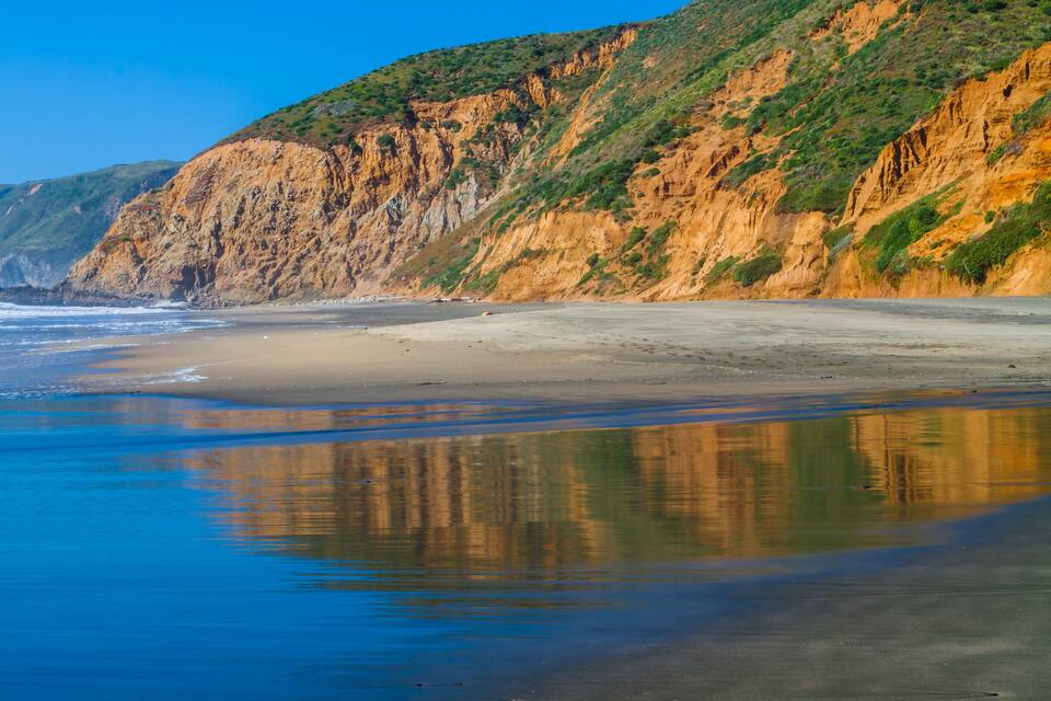 A coastal landscape with a sandy beach, cliffs, and a calm sea.