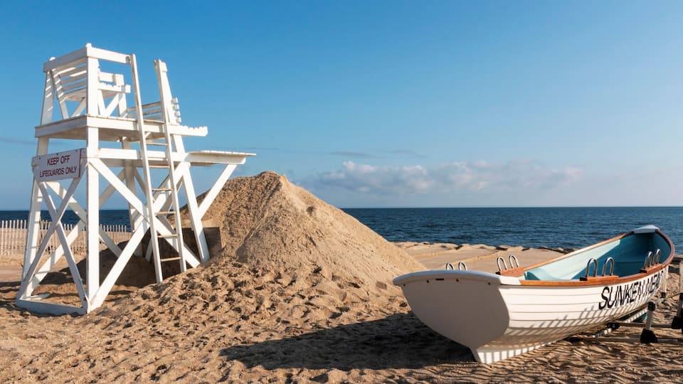 A lifeguard tower, a boat, and a sandy beach with the ocean in the background.