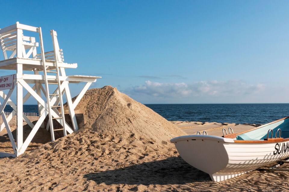 Une tour de surveillance pour les sauveteurs, un bateau et une plage de sable avec l’océan en arrière-plan.