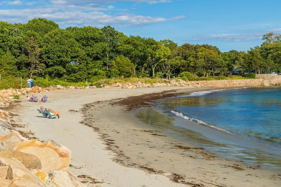 Platja sorrenca amb un mar tranquil, envoltada de vegetació verda exuberant i una paret de pedra.