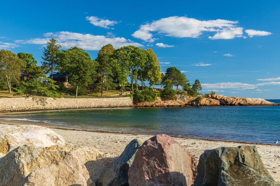 A coastal landscape with a sandy beach, rocky outcrops, and a clear blue sky.