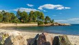 A coastal landscape with a sandy beach, rocky outcrops, and a clear blue sky.