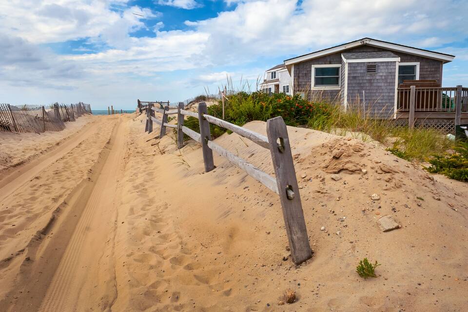 Una platja sorrenca amb una tanca de fusta, una casa i un cel serè.