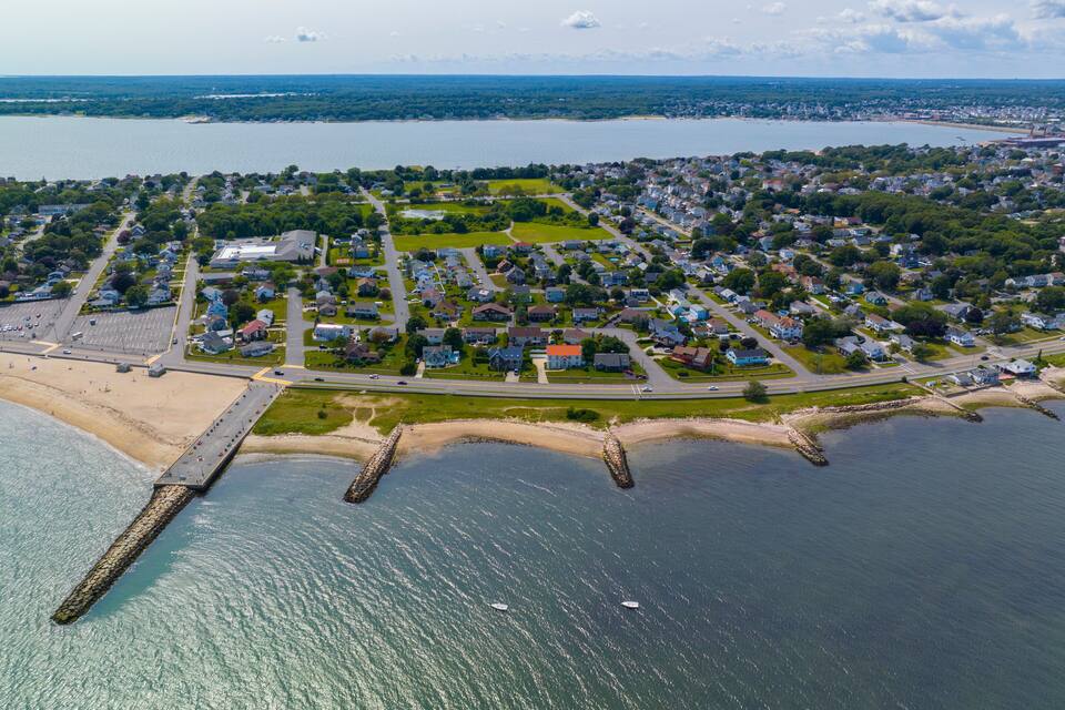 An aerial view of a coastal town with a beach, houses, and a pier.