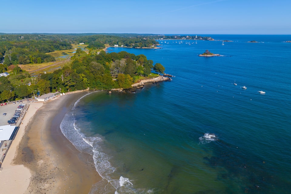 A coastal landscape with a sandy beach, clear blue waters, and a forested area.