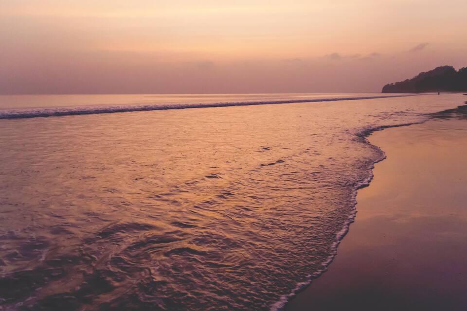 A beach at sunset with gentle waves and a calm sea.