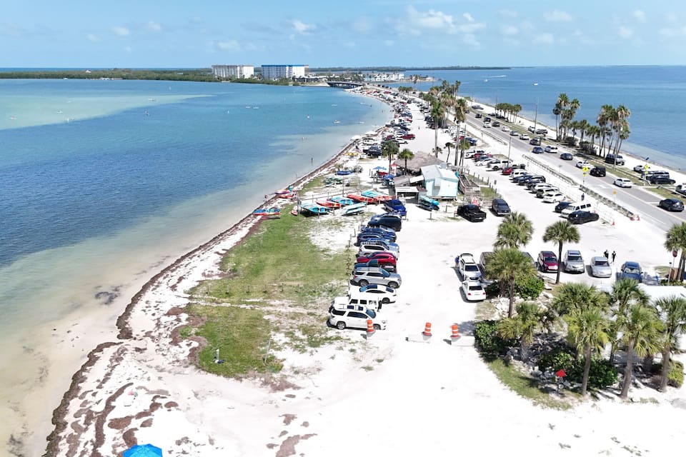 A beach with parked cars, a parking lot, and a clear view of the ocean.