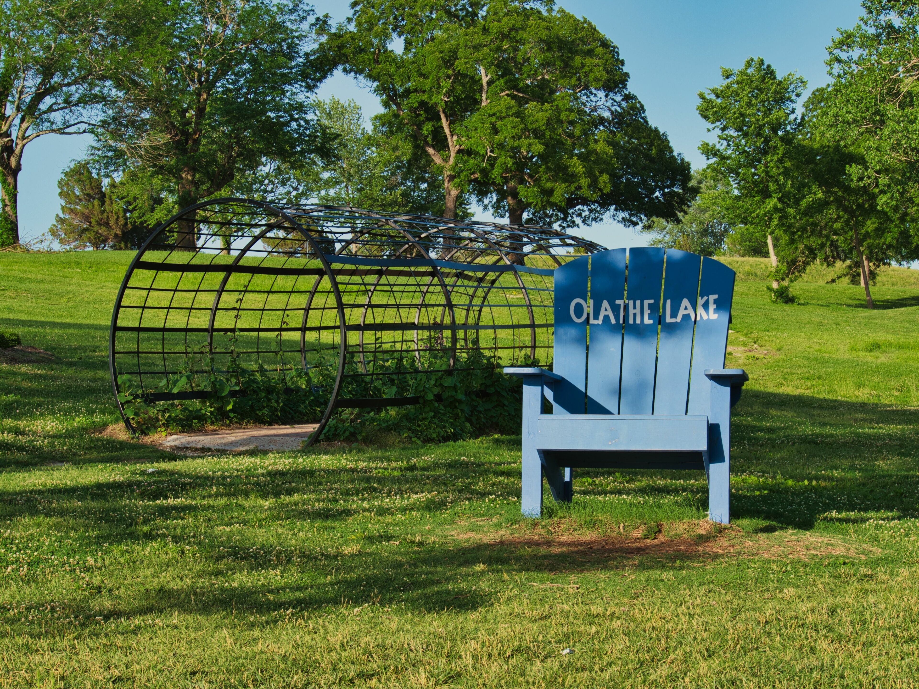 Blue wooden lawn chair near the splash pad in the green field at Olathe Lake