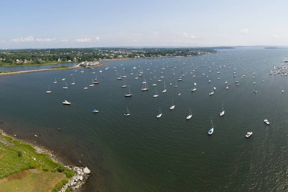 A river with numerous sailboats, surrounded by greenery and a bridge.