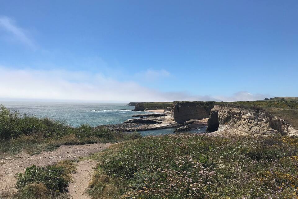 A coastal landscape with cliffs, a clear sky, and a dirt path.