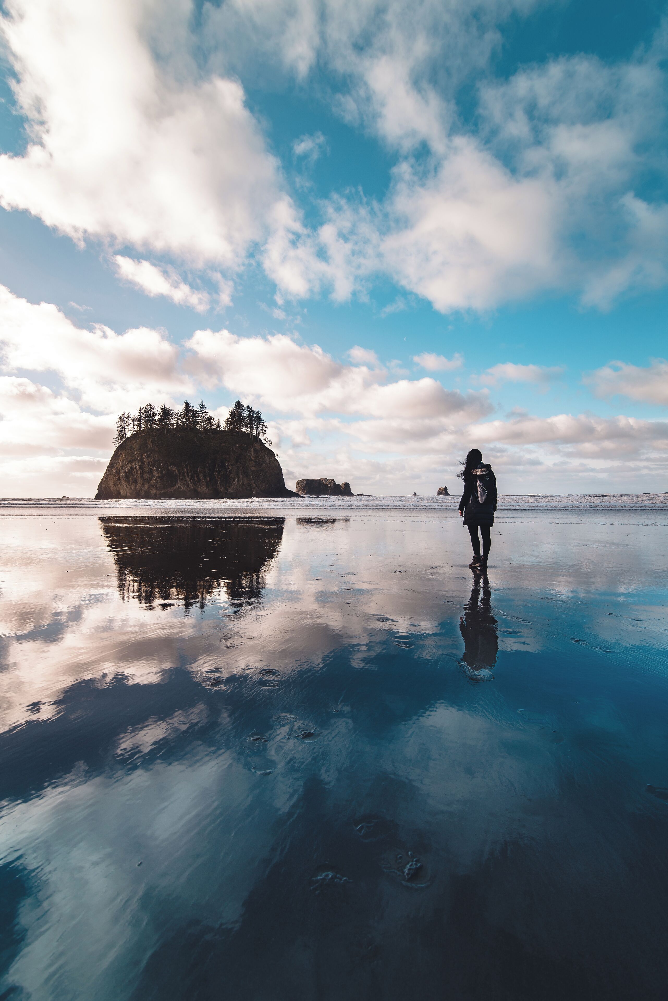 A person standing on a reflective water surface with a rocky island and trees in the background.
