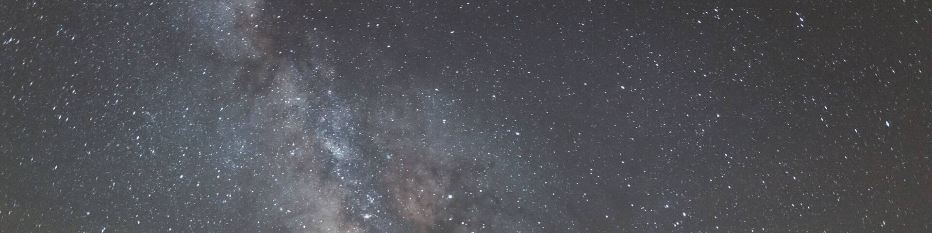 A starry night sky over a calm sea with a silhouette of a small island.